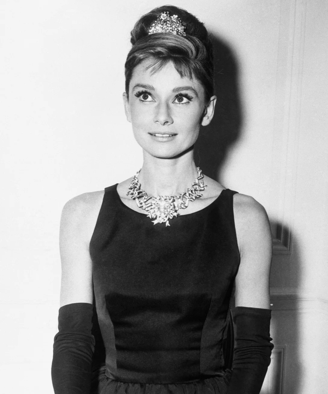 Actress Audrey Hepburn wearing her iconic Breakfast at Tiffany's black dress and gloves, diamond necklace and tiara, and hair upswept